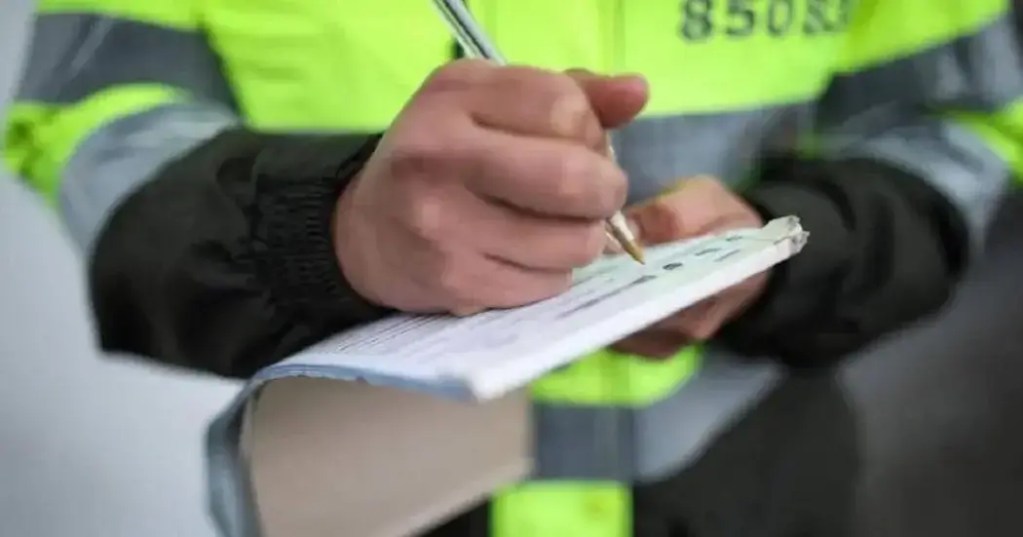 Un agente de tránsito escribe una multa en un cuaderno mientras está vestido con un uniforme reflectante.