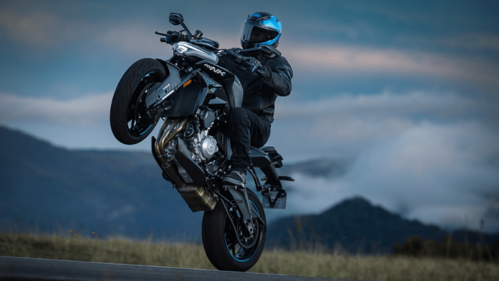 Un motociclista realiza un caballito sobre una motocicleta en un paisaje montañoso, mostrando destreza y control.