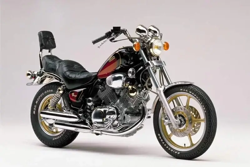 Imagen de una motocicleta Yamaha Virago con diseño custom, motor V-twin, y detalles cromados. La moto presenta un asiento bajo y estilizado, con llantas doradas y un faro frontal clásico.