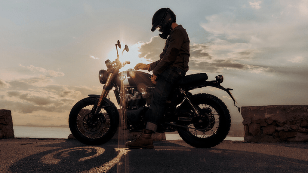 Un motociclista sentado sobre la Royal Enfield Bear 650, con un atardecer de fondo, mostrando el diseño scrambler de la moto.