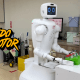 Robot Nurabot de Kawasaki en un hospital, sosteniendo bandejas médicas, con logo de Mundo Motor en primer plano.