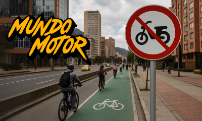 Señal de prohibición para motos eléctricas y ciclomotores en ciclorruta de Bogotá, con ciclistas circulando y edificios al fondo.