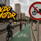 Señal de prohibición para motos eléctricas y ciclomotores en ciclorruta de Bogotá, con ciclistas circulando y edificios al fondo.