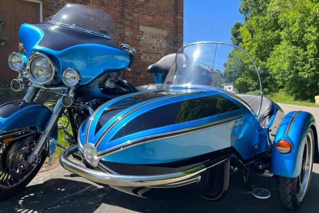 Motocicleta Harley-Davidson de color azul con sidecar, exhibida en un entorno natural y soleado.