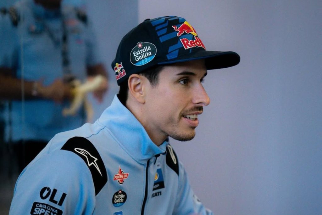 Retrato de un piloto de motociclismo con gorra, vistiendo una chaqueta de equipo, sonriendo mientras habla.