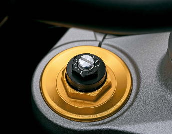 Close-up of an adjustable suspension setup knob on a motorcycle, featuring a gold-colored base and a black adjustment dial.