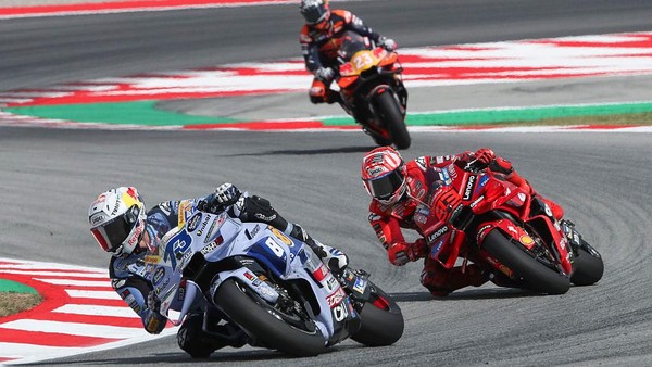 Motociclistas compitiendo en el Gran Premio de Cataluña, con un piloto de Ducati liderando la carrera mientras otros dos están en segundo y tercer lugar en la pista de Montmeló.