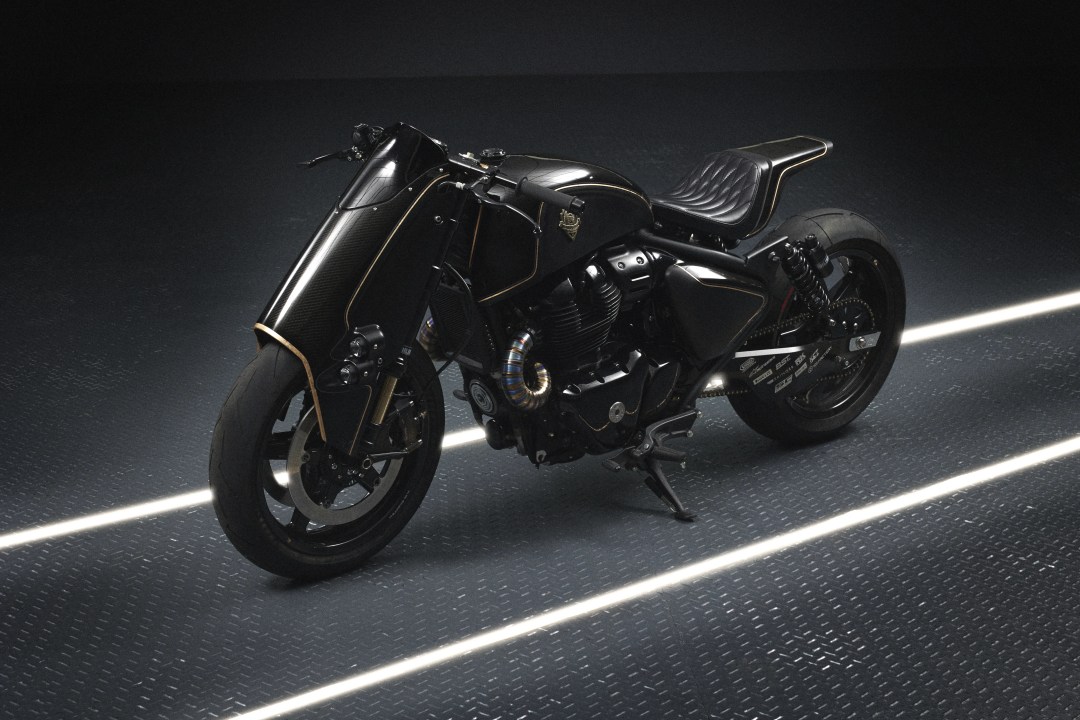 Motocicleta negra con detalles en dorado, diseñada para la edición limitada Shotgun 650 x Rough Crafts de Royal Enfield, exhibida en un entorno moderno.