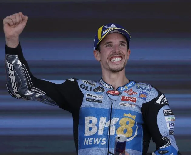 Piloto de MotoGP sonriendo y levantando el puño en señal de victoria, luciendo un traje de carreras del equipo BK8 Gresini Racing.