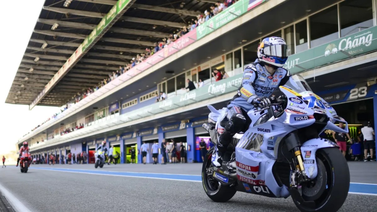 Un piloto en una moto de competición Ducati, saliendo de los boxes en un circuito de MotoGP con aficionados en las gradas al fondo.