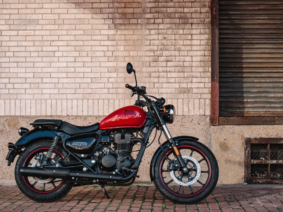 Motocicleta Royal Enfield Meteor 350 de color rojo, estacionada junto a una pared de ladrillos, con detalles en negro y llantas de estilo moderno.