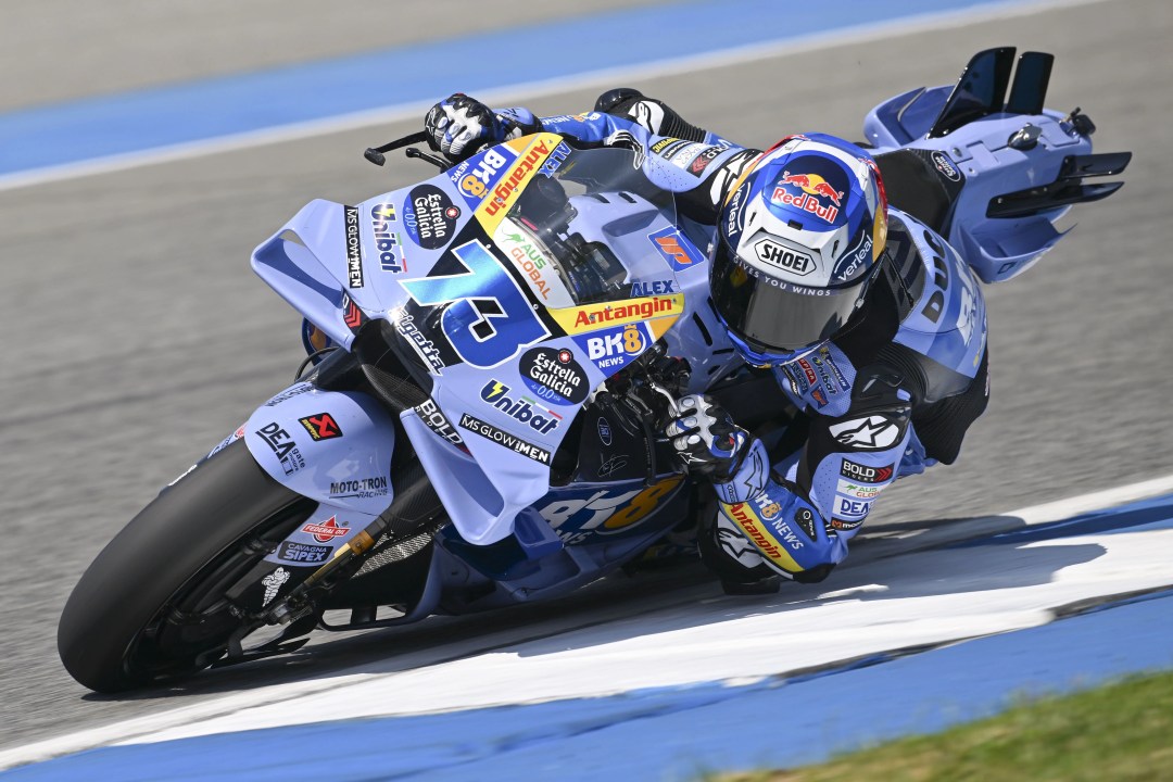 A motorcycle racer leaning into a curve on a racetrack, wearing a blue and black racing suit and a helmet. The motorcycle features prominent sponsor logos.