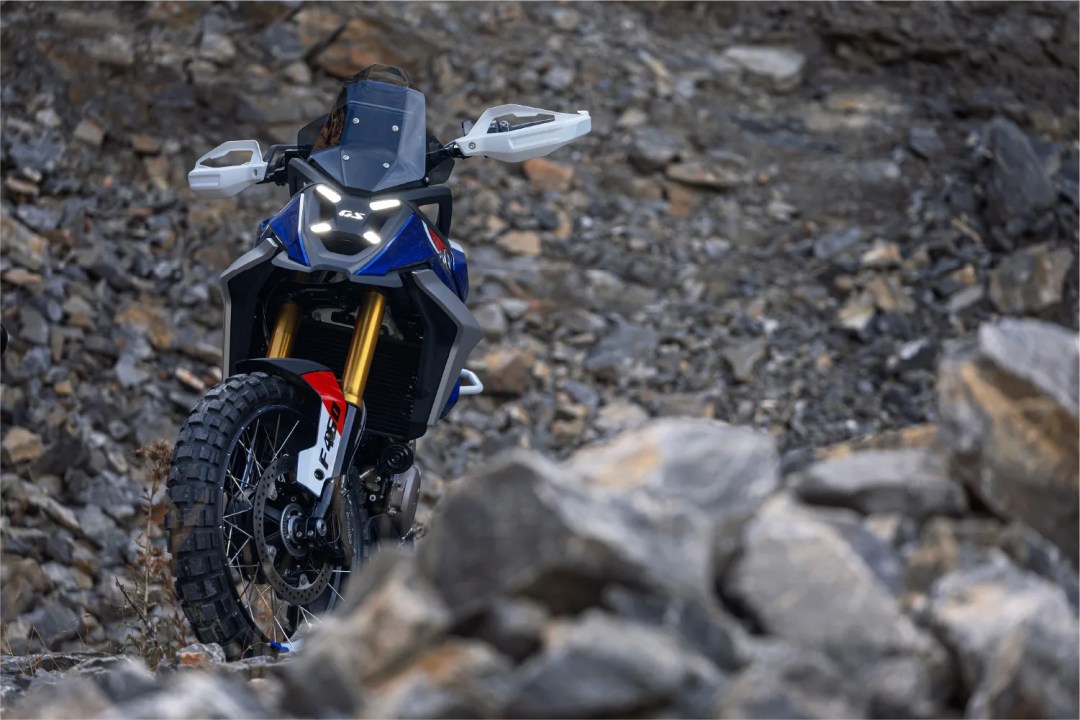 A blue and white adventure motorcycle with rugged tires, positioned on rocky terrain.