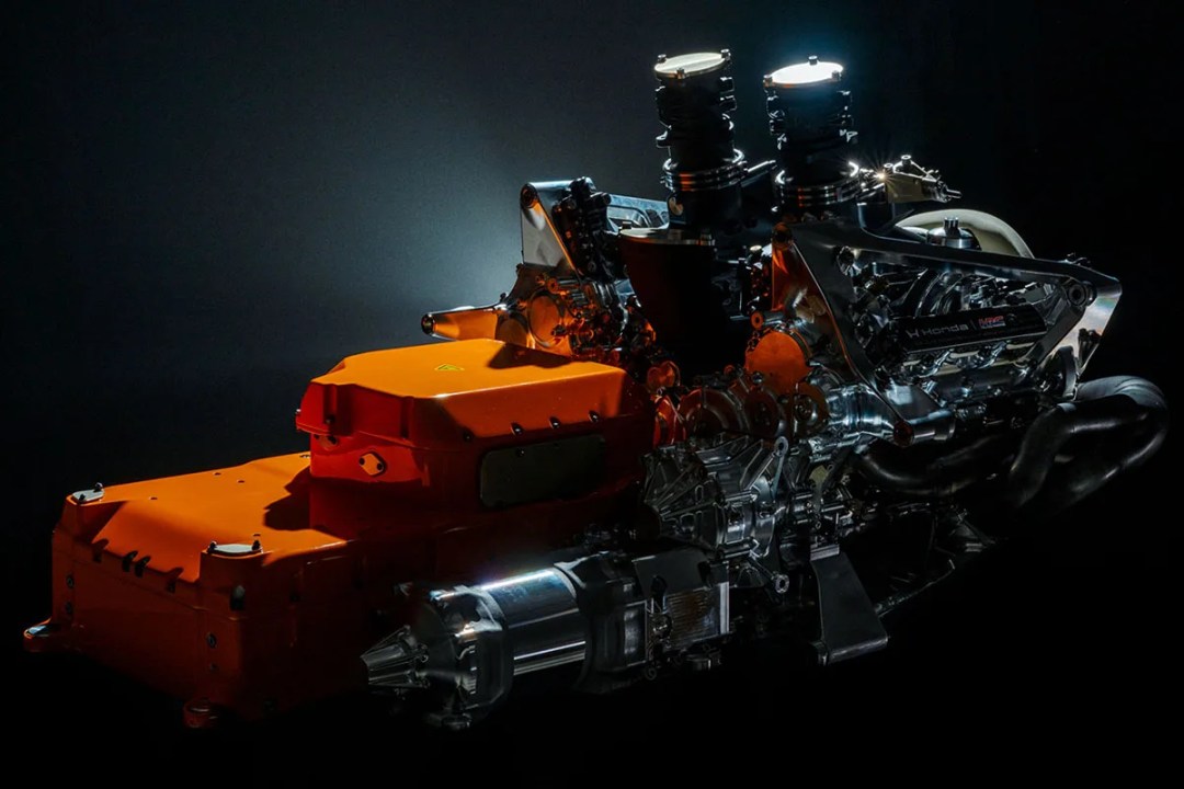 A detailed view of a modern engine, showcasing its metallic components, orange casing, and illuminated sections against a dark background.