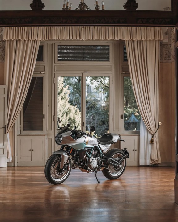 A stylish Ducati Formula 73 (2026) motorcycle positioned inside an elegant room with large windows and draped curtains.