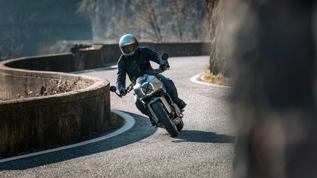 A motorcyclist in a helmet riding a Ducati Formula 73 (2026) motorcycle around a winding road with a scenic landscape in the background.