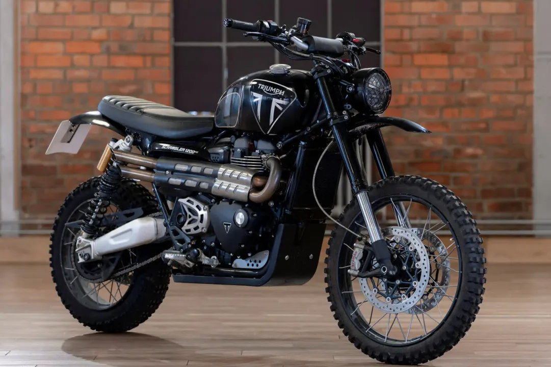 Motocicleta Triumph Scrambler negra en un ambiente moderno con fondo de ladrillos.