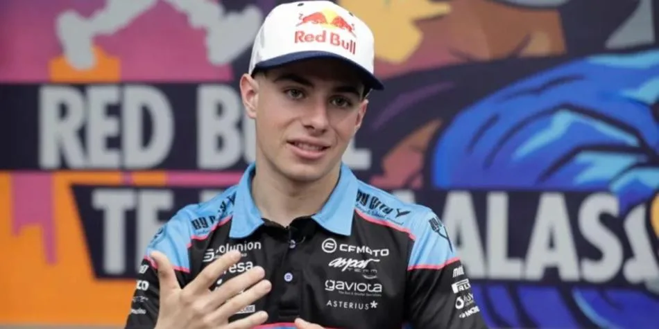 A young man wearing a Red Bull cap and a branded racing shirt gestures while speaking in front of a colorful mural.