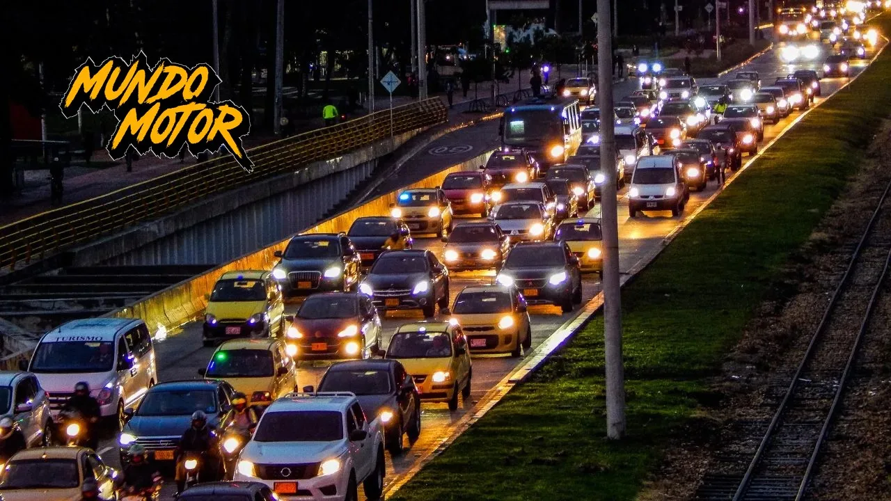 Tráfico nocturno en una avenida colombiana con carros y motociclistas con casco circulando entre los vehículos, con el logo de Mundo Motor