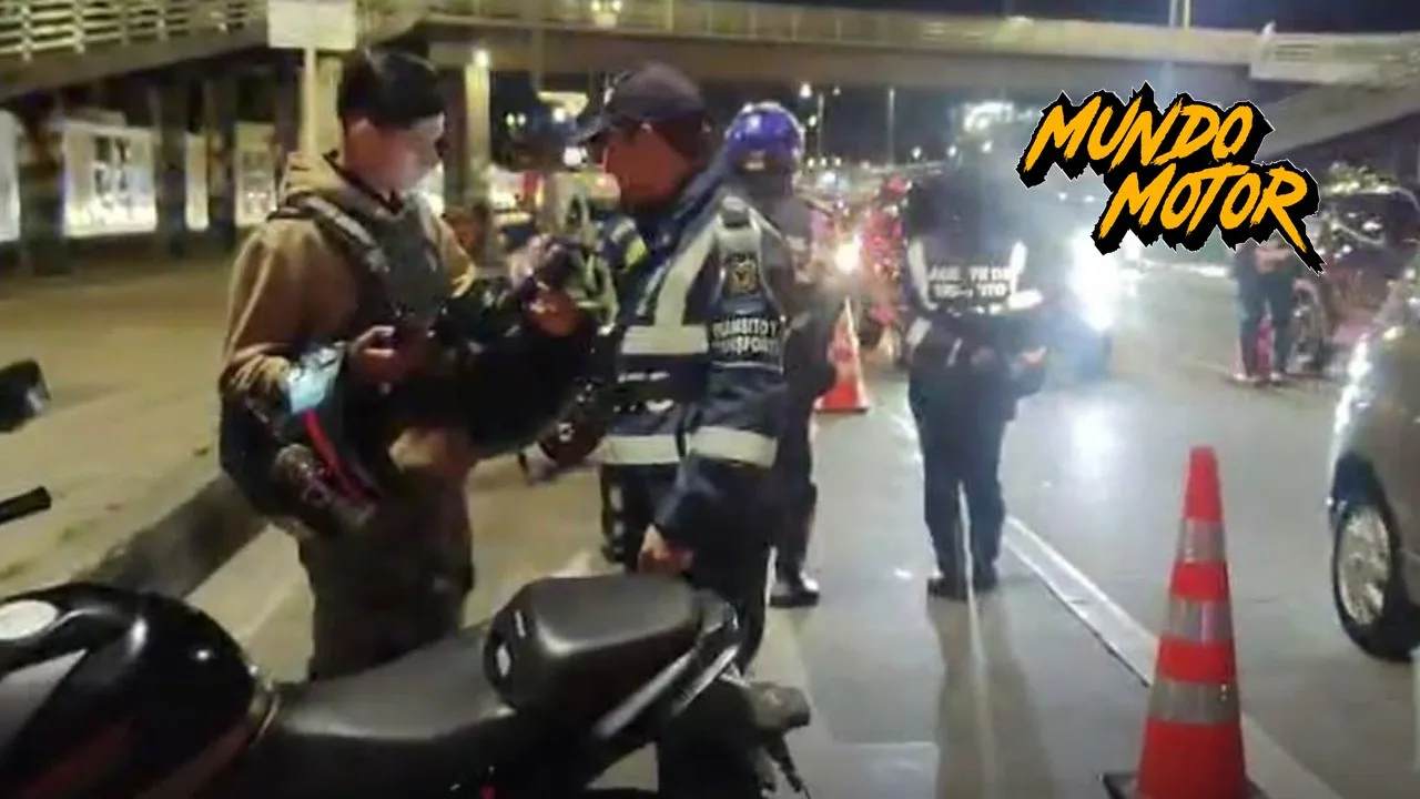 Agentes de tránsito revisan a un motociclista en un puesto de control nocturno en Bogotá durante las restricciones de Halloween, con el logo de Mundo Motor